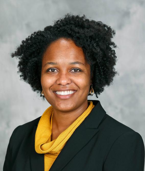 Portrait photo of Stephanie Davis smiling in a black blazer with a gold top