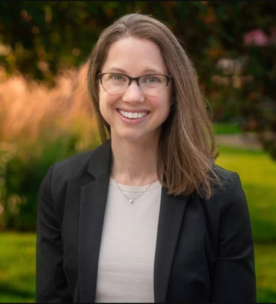 Christiana Raymond-Pope smiling in white top with black blazer before natural background