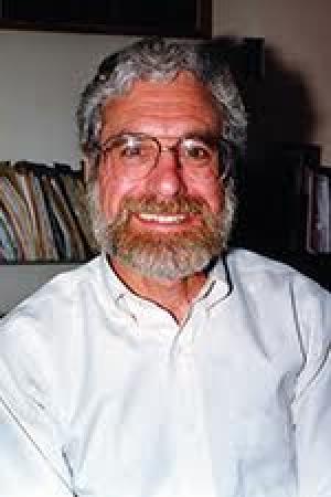 portrait image of Professor Emeritus Leo McAvoy in white shirt, full beard and glasses before a bookshelf