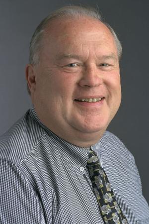 Professor Emeritus, Bob Serfass, in portrait, smiling in a blue striped shirt and tie